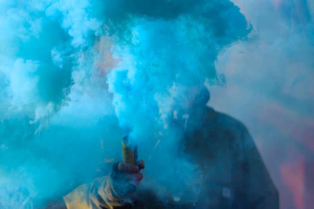 Blue smoke obscures the face of a person behind