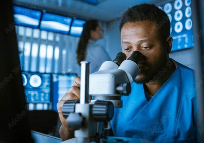 A person sits while studying something through a microscope