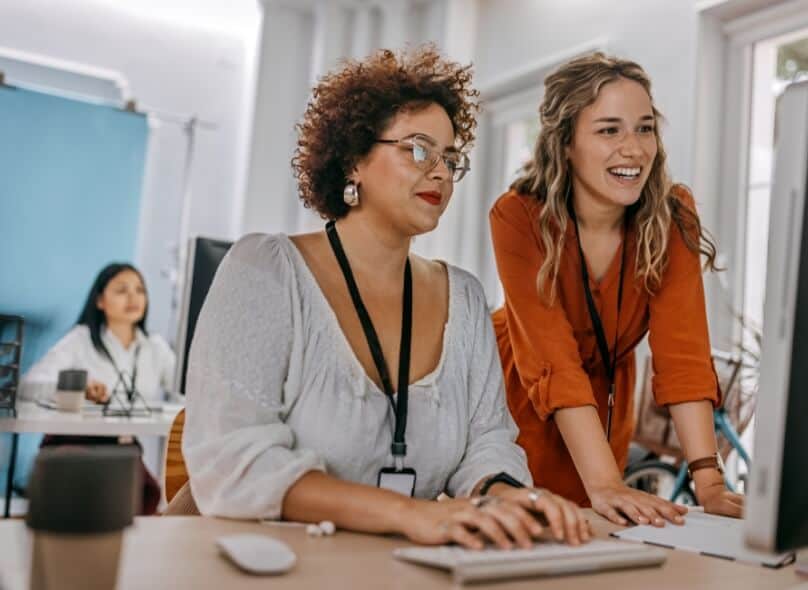 Two people at a desk smiling and looking at a computer screen