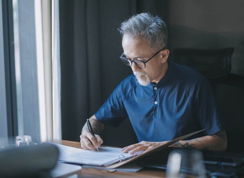 A person sits at a desk writing something in a binder