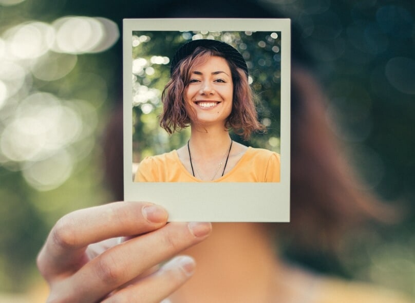 A woman holds up a polaroid of herself in front of her face