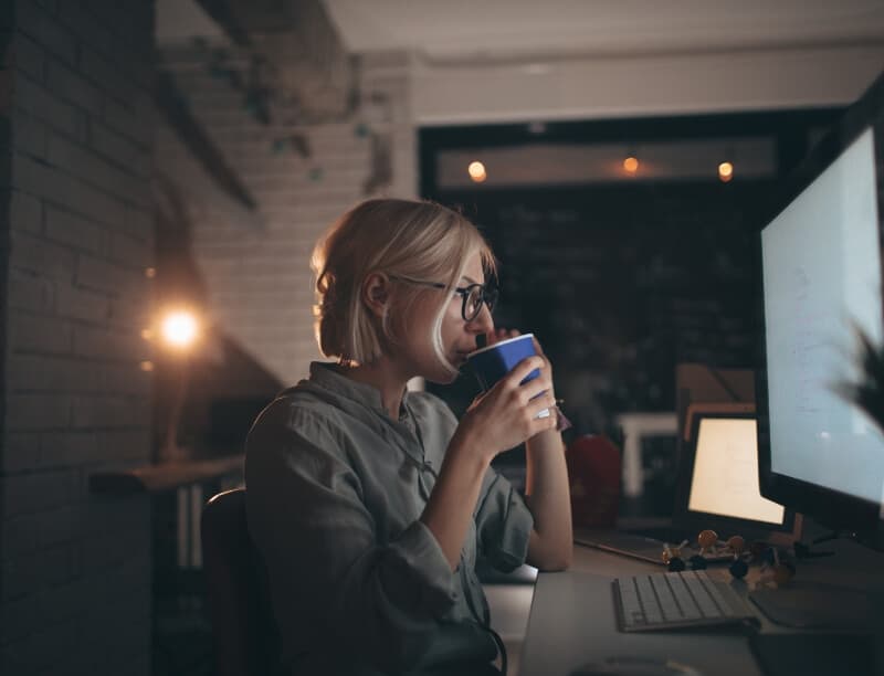 A woman drinks coffee in front of a computer screen